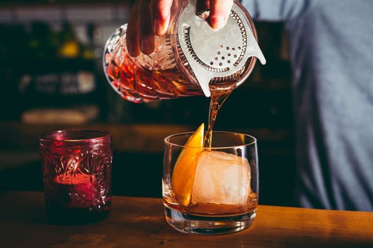 A negroni is poured over a large ice cube in a bar in Cornwall