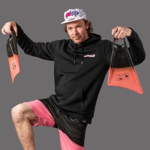 A creative studio product photographer pf a man wearing a cap, shorts and hoodie holding a pair of swiimfins.