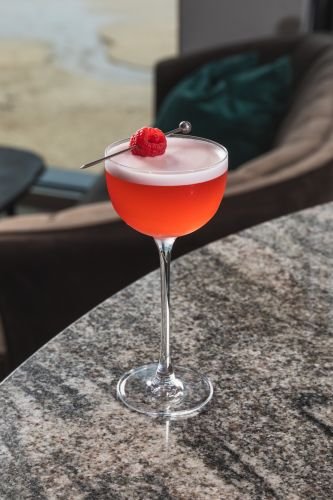 A raspberry gin cocktail with a raspberry garnish on a bar captured by a drinks photographer in Cornwall.