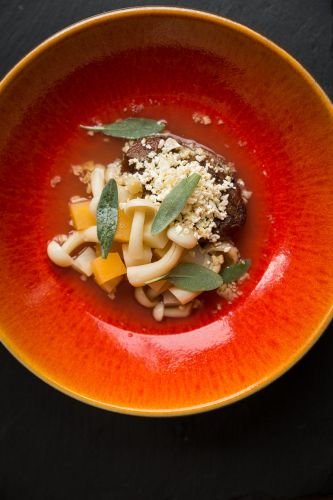 A food photographer in Cornwall captures a vibrant orange bowl filled with mushrooms, diced squash, a perfectly crafted meatball, herbs, and crumbled cheese, all beautifully nestled in a red bowl.
