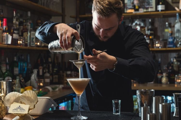 A bartender carefully strains a cocktail into a martini glass, all captured perfectly by a skilled drinks photographer in Cornwall.